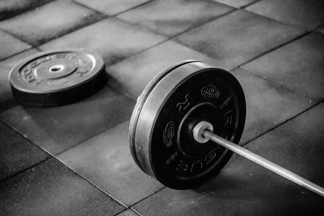 A barbell on a gym floor in a second-hand gym, depicted in black and white.