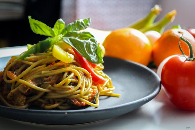A plate of spaghetti with colorful vegetables and juicy tomatoes